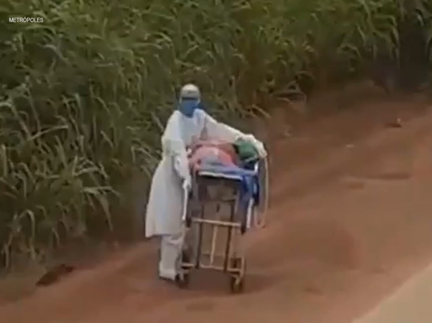 Enfermeira leva maca com paciente de Covid-19 em estrada de terra