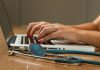 Jogos no Brasil: regulamentação amplia discussão sobre recursos para Santas Casas e saúde pública Mãos com unhas pintadas de vermelho digitando no teclado de um notebook, com um estetoscópio azul em primeiro plano sobre uma mesa de madeira.